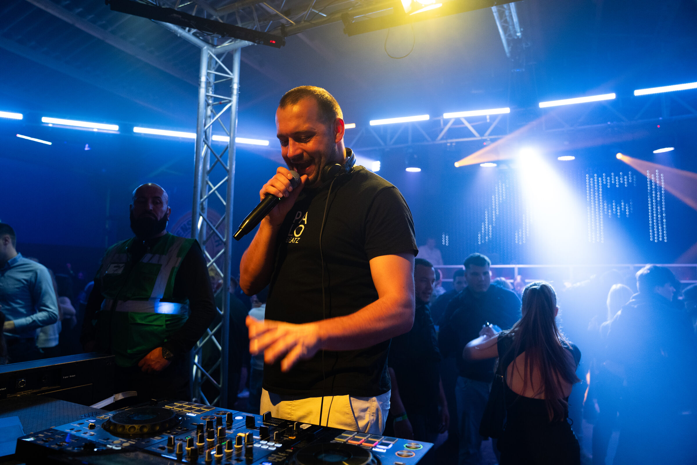 Oliver Groß lächelt mit Mikro am Pult, blaues Licht